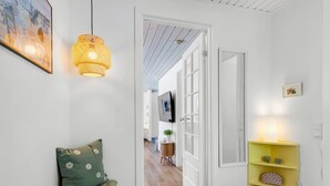 Um corredor com um sofá verde, uma prateleira amarela com objetos decorativos e um quadro na parede.