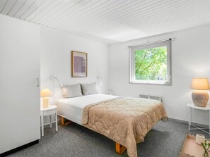 Un dormitorio con cama, mesitas de noche, ventana con vistas a zonas verdes y un cuadro en la pared.