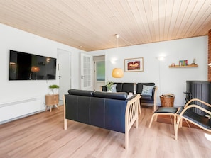 Una sala de estar moderna con sofá, sillones, televisor, chimenea y techo de madera.