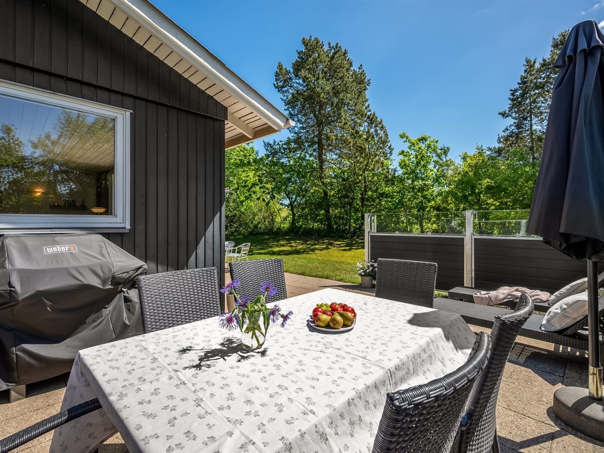 An outdoor patio with a table set for dining, surrounded by wicker chairs and a grill.