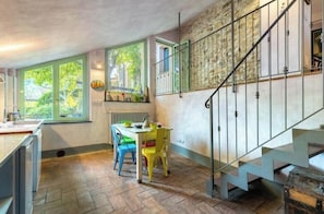 Eine Küche mit Esstisch, Stühlen, einer Treppe und einem Fenster mit Blick auf Grünflächen.