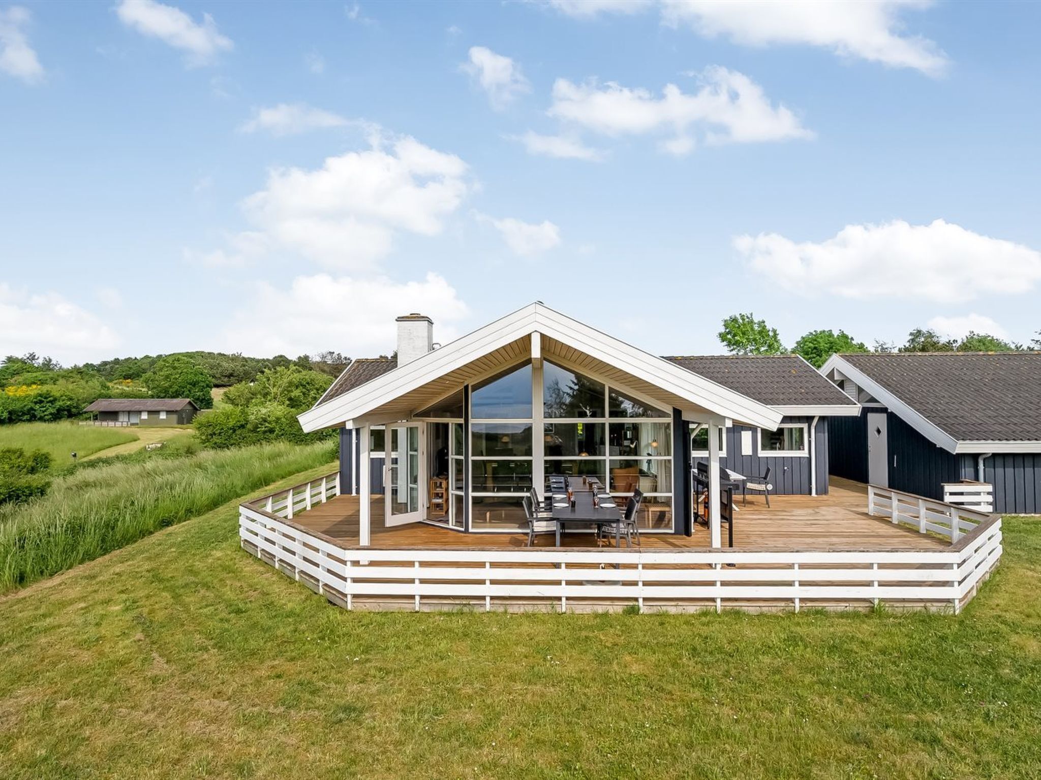 A modern house with a large deck, a covered outdoor dining area, and a view of the surrounding landscape.