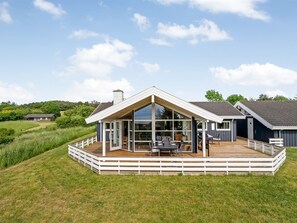 Ein modernes Haus mit einer großen Terrasse, einem überdachten Essbereich im Freien und Blick auf die umliegende Landschaft.