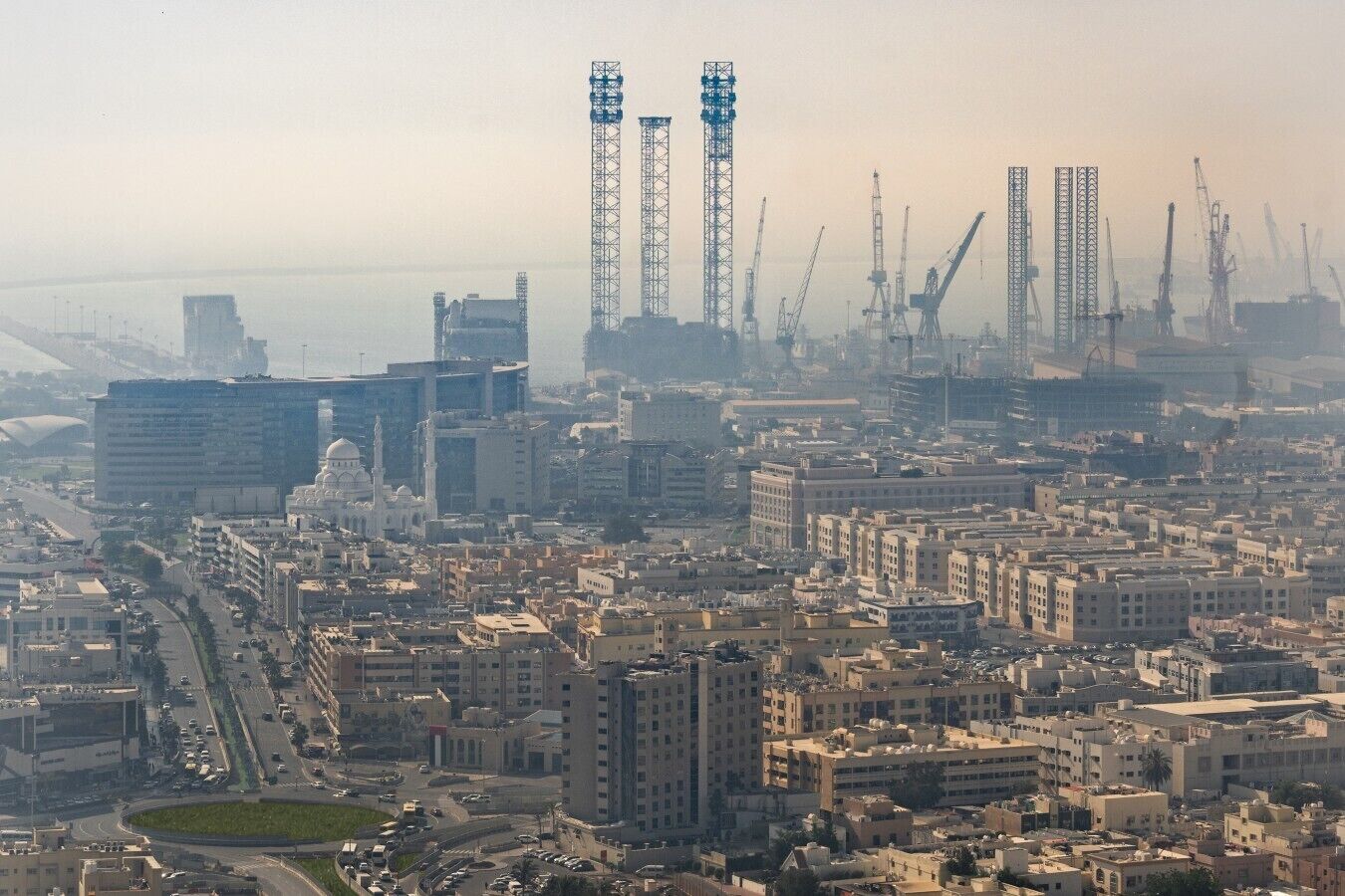 Un paysage urbain avec une mosquée imposante, divers bâtiments et des grues de construction.
