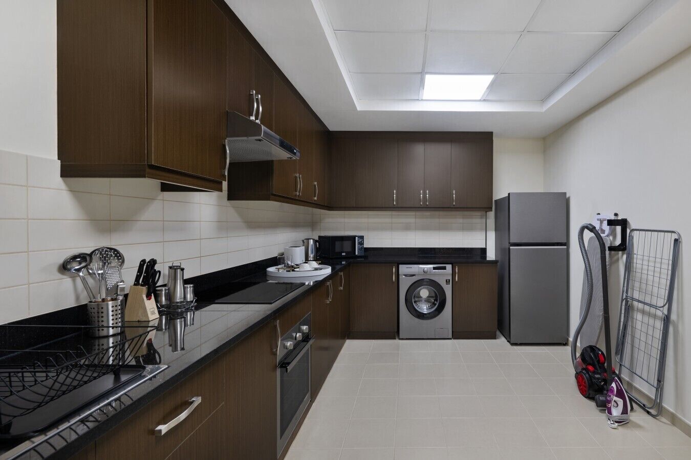 A modern kitchen with dark wooden cabinets, a built-in dishwasher, a washing machine, and a refrigerator.