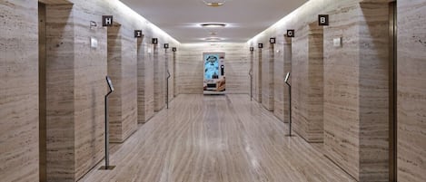 Un hall d’ascenseur moderne avec des murs et des sols en marbre, des portes numérotées et un luminaire central.
