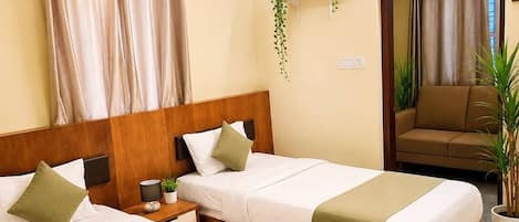 Quarto de hotel com duas camas, ventoinha no teto, espelho, sofá e uma pequena planta.