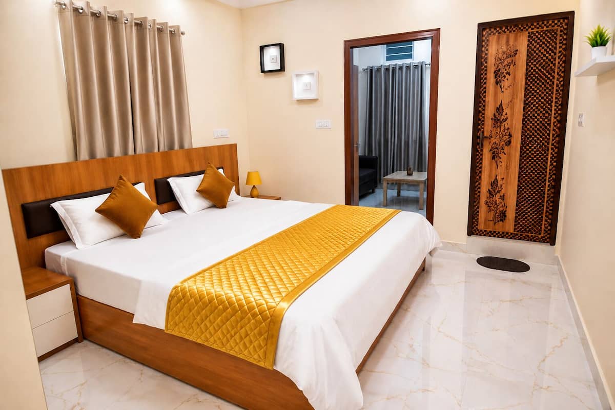 A hotel room with a large bed, a wooden headboard, a bedside table, a nightstand, a mirror, a door with intricate woodwork, and a small potted plant.