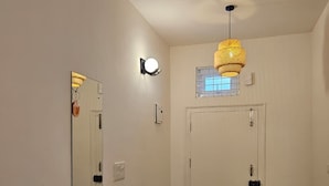 A hallway with a white door, a wall-mounted light fixture, and a mirror reflecting part of the room. - Ferro Livingz (Bengaluru)