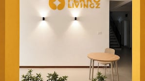 A modern interior with a round table and chairs, a wall-mounted logo, and a staircase in the background. - Ferro Livingz (Bengaluru)