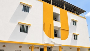 A modern building with a white facade and yellow accents, featuring multiple windows and a visible entrance. - Ferro Livingz (Bengaluru)