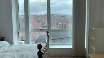 A bedroom with a large window, a bed, a wooden table, and a radiator.
