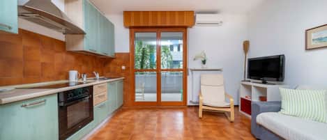 A compact kitchen with a stove, oven, and cabinets, a dining area with a chair, a sofa, and a TV.