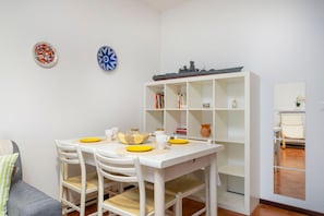 Un coin repas avec une table blanche, quatre chaises et une bibliothèque contenant des livres et des objets décoratifs.