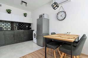 Eine moderne Küche mit Einbauwaschmaschine, Kühlschrank und Essbereich mit Holztisch und grauen Stühlen.