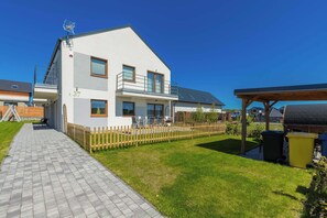 Ein modernes, zweigeschossiges Haus mit befestigter Auffahrt, Holzzaun und einer überdachten Sitzgelegenheit im Freien.