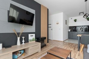 Ein modernes Wohnzimmer mit Flachbildfernseher, Holzmöbeln, einer schwarzen Unterhaltungseinheit und einer Küche im Hintergrund.