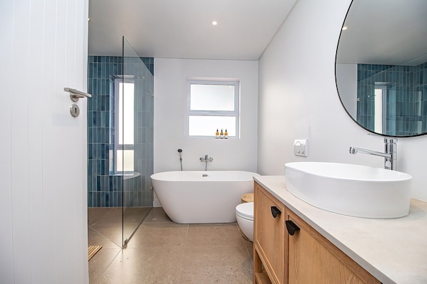 Un baño moderno con una bañera independiente, un espejo grande y una ventana sobre el lavamanos.