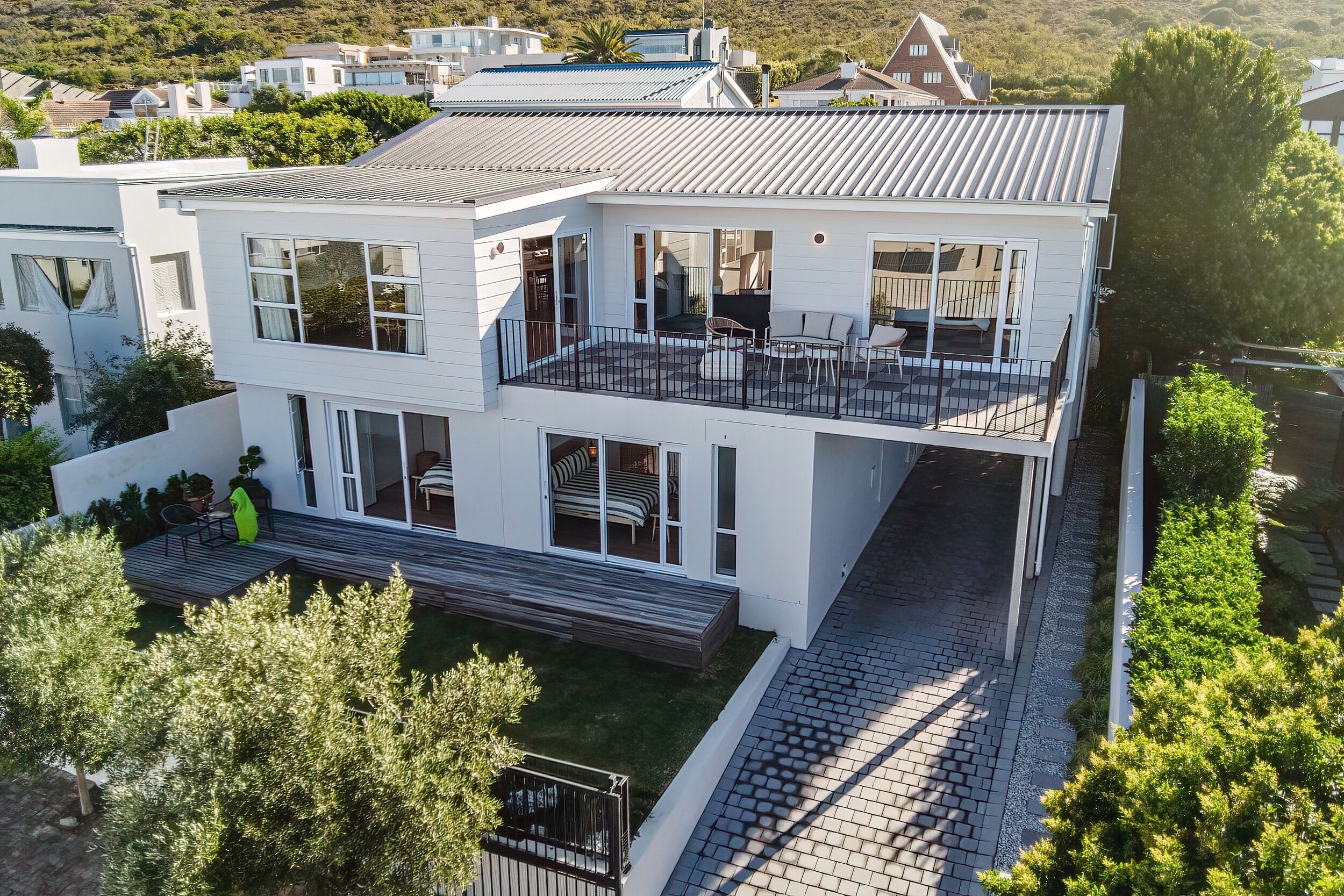 A modern two-story house with a balcony, large windows, and a paved driveway.