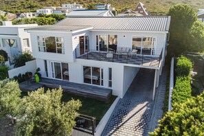 A modern two-story house with a balcony, large windows, and a paved driveway. - Legacy House | Sea and mountain views | Voelklip (Hermanus)