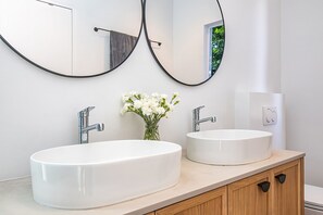 A bathroom with two sinks, a mirror, and a vase of flowers. - Legacy Villa | Voelklip | Sea & mountain views (Hermanus)