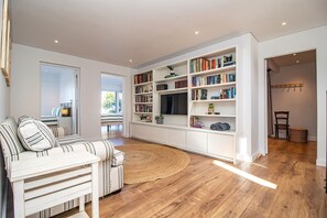 A modern living room with a sofa, a large bookshelf, and a TV. - Legacy Villa | Voelklip | Sea & mountain views (Hermanus)
