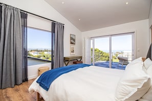 A bedroom with a bed, a desk, a chair, and a view of the outside. - Legacy House | Sea and mountain views | Voelklip (Hermanus)