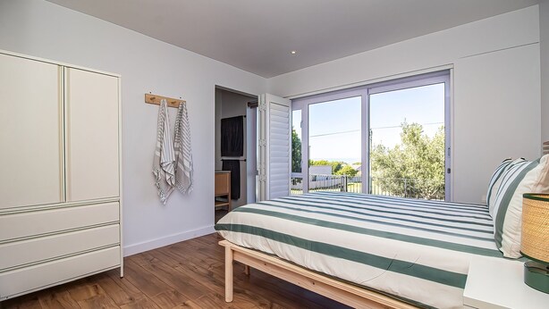 Een slaapkamer met een bed, een kledingkast, een bankje, een raam en uitzicht op het omliggende landschap.