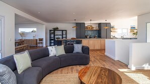 Een moderne woonkamer met een gebogen bank, een houten salontafel en een keuken op de achtergrond.