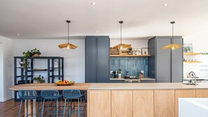 Een moderne keuken met een centraal eiland, barkrukken, hanglampen en een geïntegreerde kookplaat.