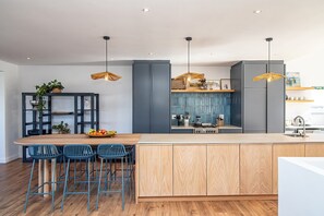 A modern kitchen with a central island, bar stools, pendant lights, and a built-in stove. - Legacy House | Sea and mountain views | Voelklip (Hermanus)