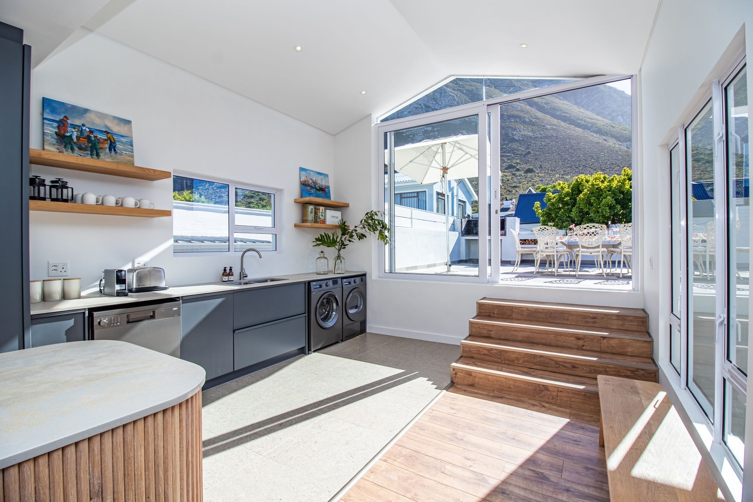 A modern kitchen with built-in appliances, a dining area with outdoor seating, and a large window offering a view of the outdoors.
