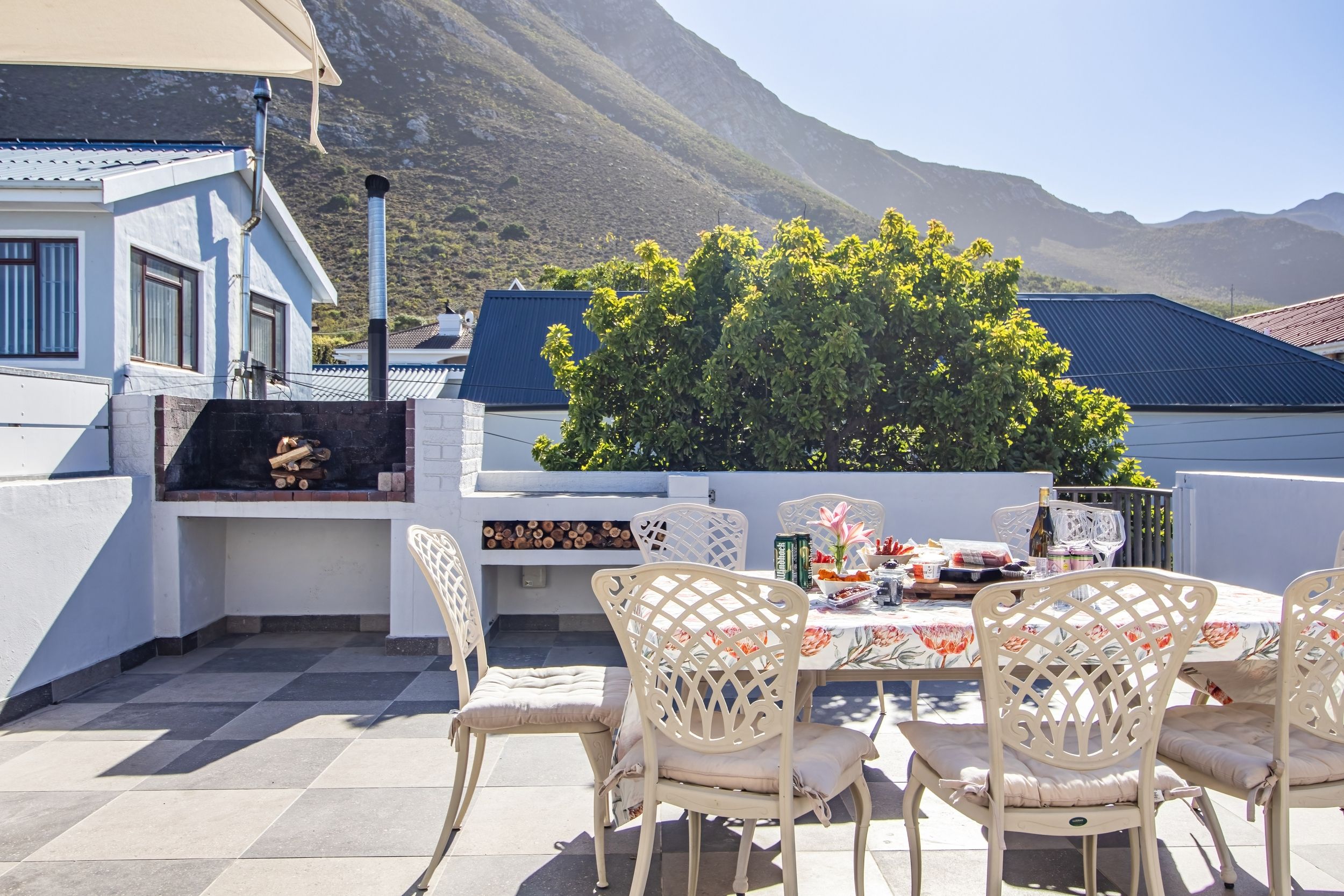 Un patio al aire libre con una mesa lista para comer, rodeado de sillas blancas y una parrilla.
