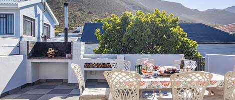 An outdoor patio with a table set for dining, surrounded by white chairs, and a barbecue grill.