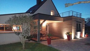 Una casa moderna de dos pisos con balcón, un patio con mobiliario exterior y un césped bien cuidado.