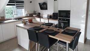 Una cocina moderna con armarios blancos, una isla de madera, sillas negras y un televisor de pantalla plana montado sobre el microondas.
