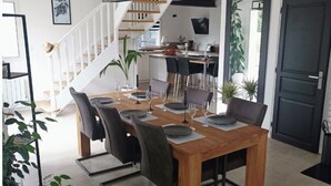Un comedor con una mesa y sillas de madera, una escalera y una cocina al fondo.