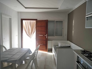 Una habitación pequeña con mesa de comedor, cama, kitchenette y ventana con cortinas.