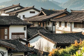 Edificios tradicionales con varios tejados y un paisaje montañoso de fondo.