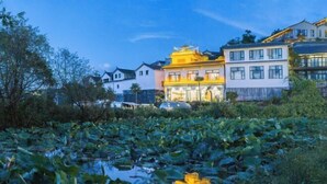 A hotel with traditional architecture, a pond with lily pads, and a reflection of the building. - Yugui Hot Spring Holiday Hotel (Tengchong)