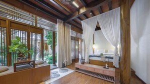 A bedroom with a wooden floor, a bed with white curtains, a bedside table, and a potted plant. - Yugui Hot Spring Holiday Hotel (Tengchong)