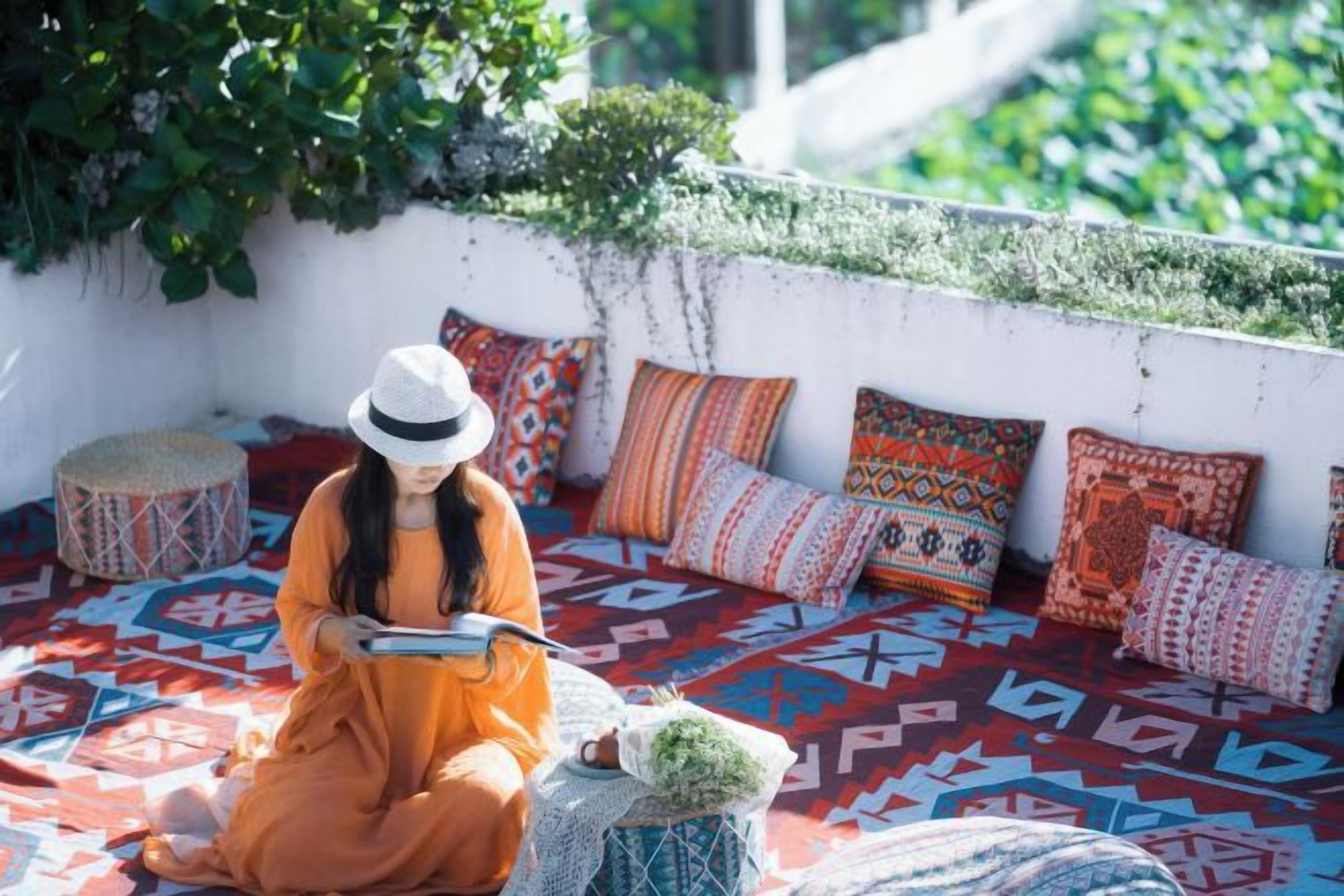 A person sitting on a patterned sofa with cushions, reading a book.