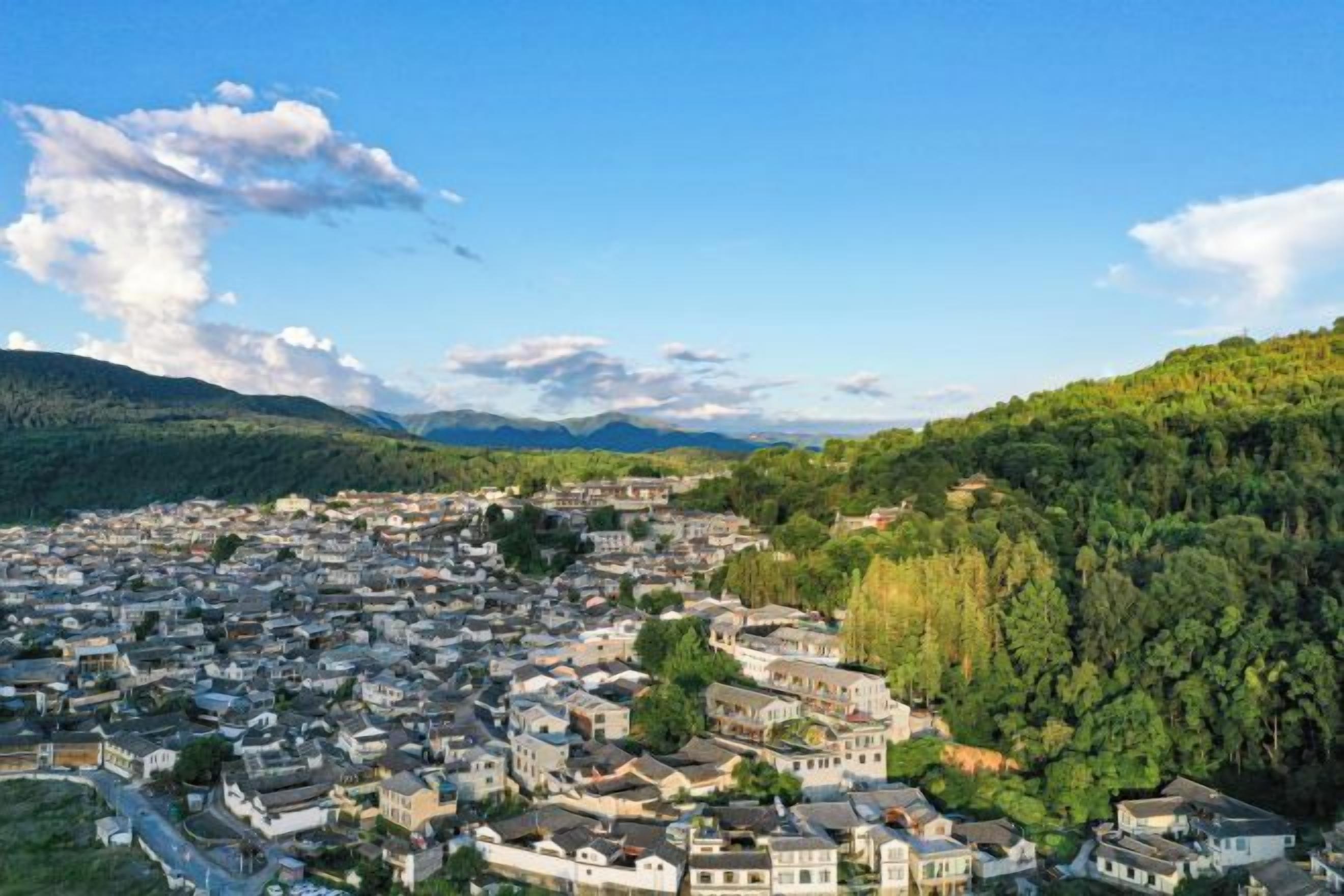 A town with a mix of traditional and modern buildings, surrounded by hills and greenery.