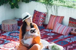 Una persona sentada sobre un suelo estampado con cojines de colores, sosteniendo un gato.