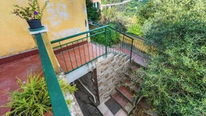 A staircase with a green railing leading to a balcony, surrounded by greenery and a yellow wall. - Hostdomus - Oltrefinale (Liguria)