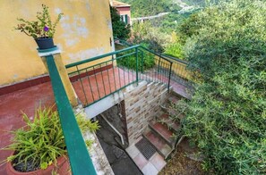 Escada com corrimão verde que leva a uma varanda, cercada por vegetação e uma parede amarela.