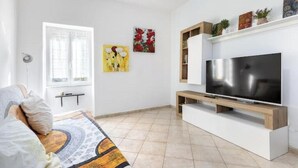 A living room with a TV, a sofa, a window, and artwork on the wall. - Hostdomus - Oltrefinale (Liguria)
