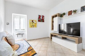 Uma sala de estar com televisão, sofá, janela e obras de arte na parede.