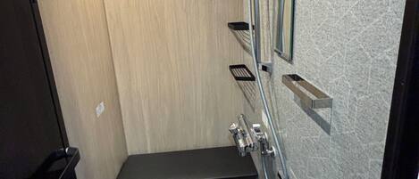 A compact shower area with a bench, a handrail, and a wall-mounted mirror.