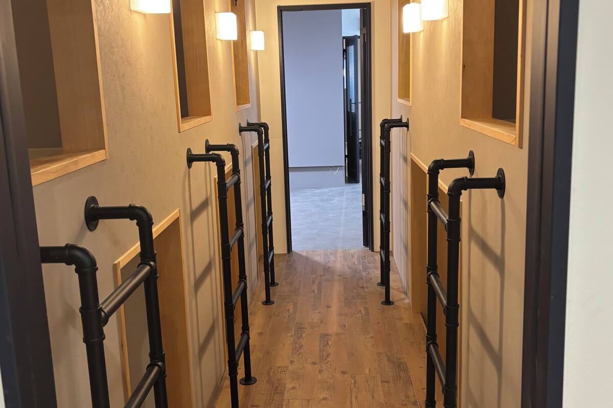 A hallway with black metal railings, wooden flooring, and wall-mounted light fixtures.